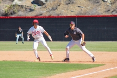 Palomar baseball player in white leans to the left while Saddleback's first baseman also leans left as the two wait for the outcome of the next pitch.