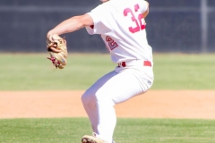Baseball player in a white uniform and cap pitching on a baseball field during a game, with his leg lifted mid-throw on the pitcher’s mound.