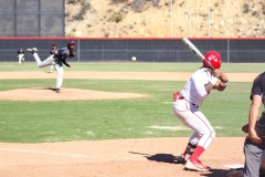 Palomar baseball player in white and red prepares to swing at an incoming pitch from Saddleback's pitcher.