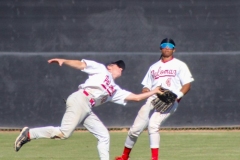 As outfielder in a white uniform reaches out to catch the baseball while almost colliding with another outfielder in a white uniform.