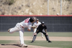 A baseball player in a white Palomar uniform has his body twisted as he has already pitched the ball.