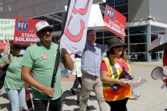 Carmelino Cruz (in green), Anel Gonzalez (in the safety vest), and Lawrence Lawson (in the plaid shirt) lead the march in solidarity for community college students and workers on March 12, 2026. 