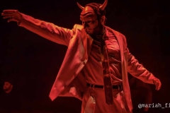 Lucifer (Owen Hall) stretches an arm across the stage, bathed in red light, as he rallies his demons in "Pastorela Fronteriza." (Photo Courtesy of Mariah Lambert)