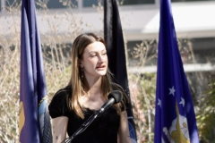 A woman with dirty blond hair is standing behind the podium and is singing the National Anthem.