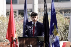 A man in a blue suit and red tie stands behind the podium reciting the Pledge of Allegiance.