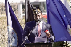 A man in a navy blue suit and Navy hat stands behind the podium giving a speech.