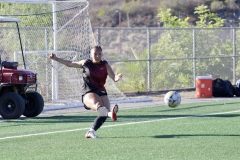 Karlena Tamayo (#19) in black kicks the ball to her teammates near the goal.