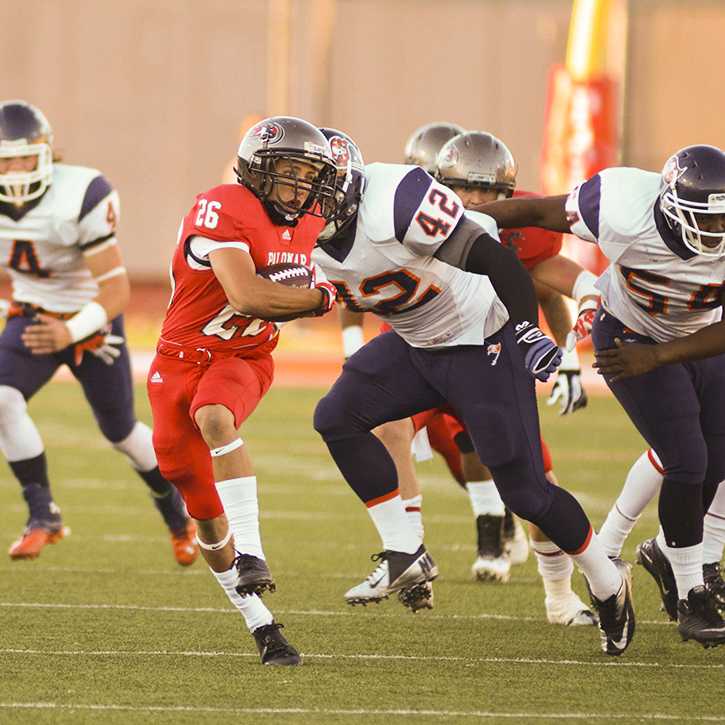 A Palomar football player runs with a football tucked in his right arm as several opposing players chase him from behind.