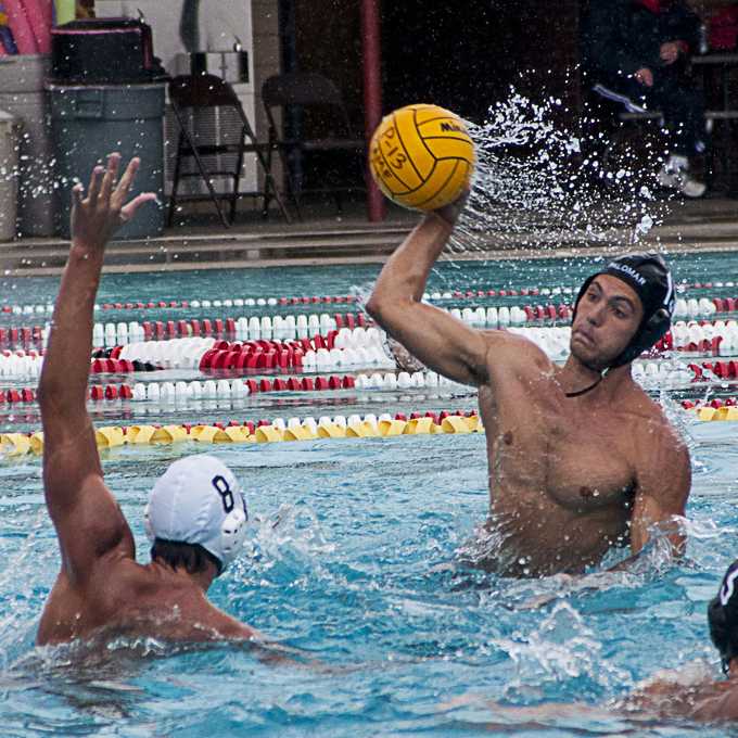 A male Palomar water polo player tries to throw a ball from as an opponent tries to block him with his left arm.