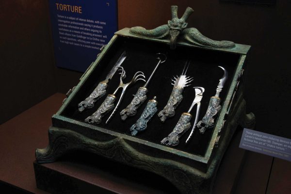 Seven small torture tools that has sharp spikes, hooks, or blades lie inside an old, greenish metal box.