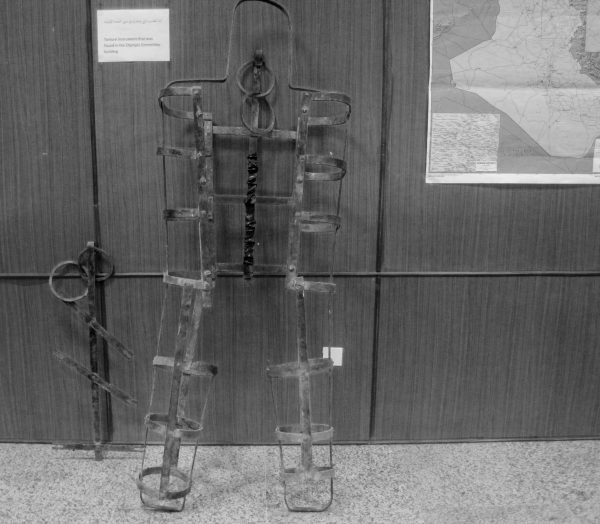 A metal contraption in a rough shape of a human stands against a wall.