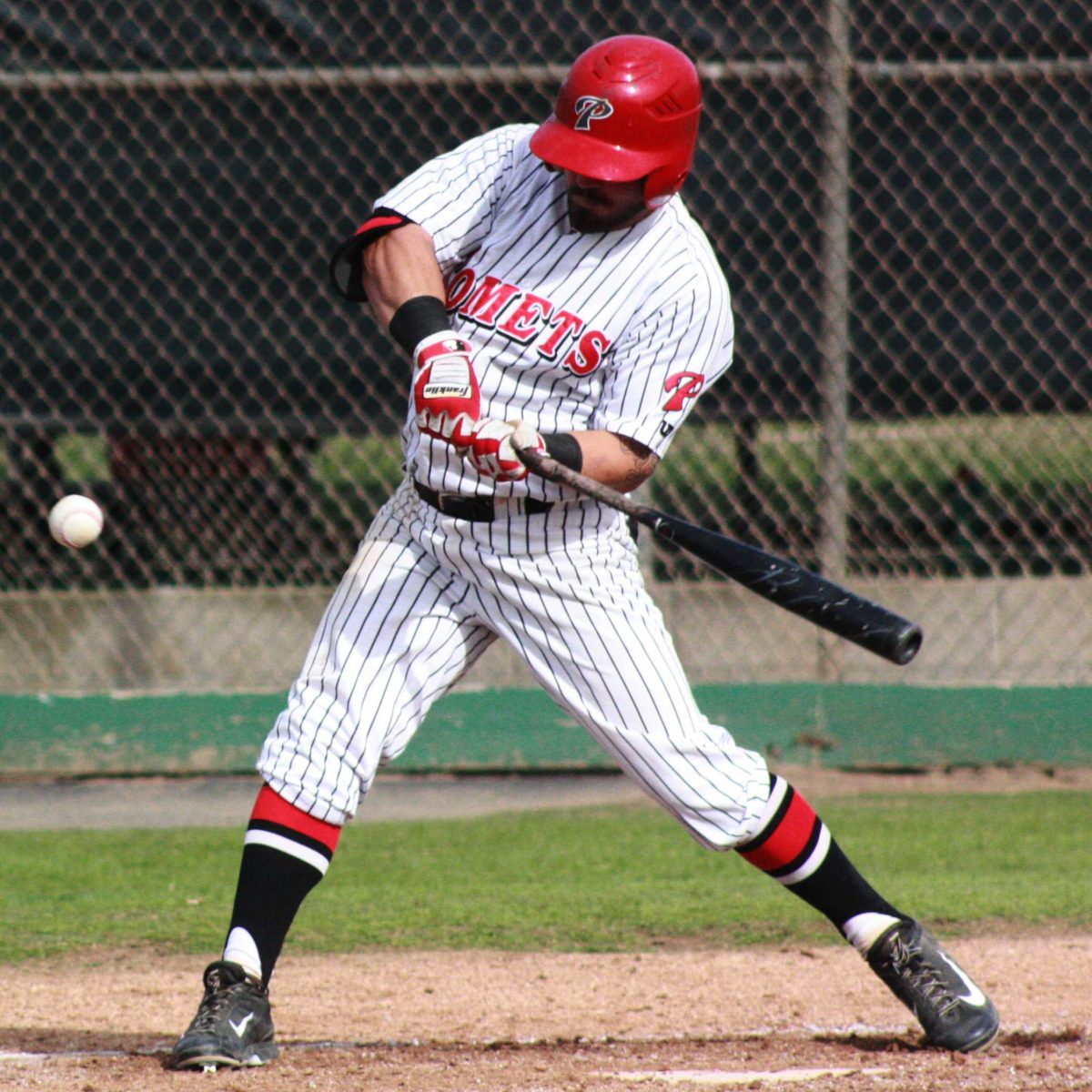 A male Palomar baseball swings a bat at an incoming baseball.