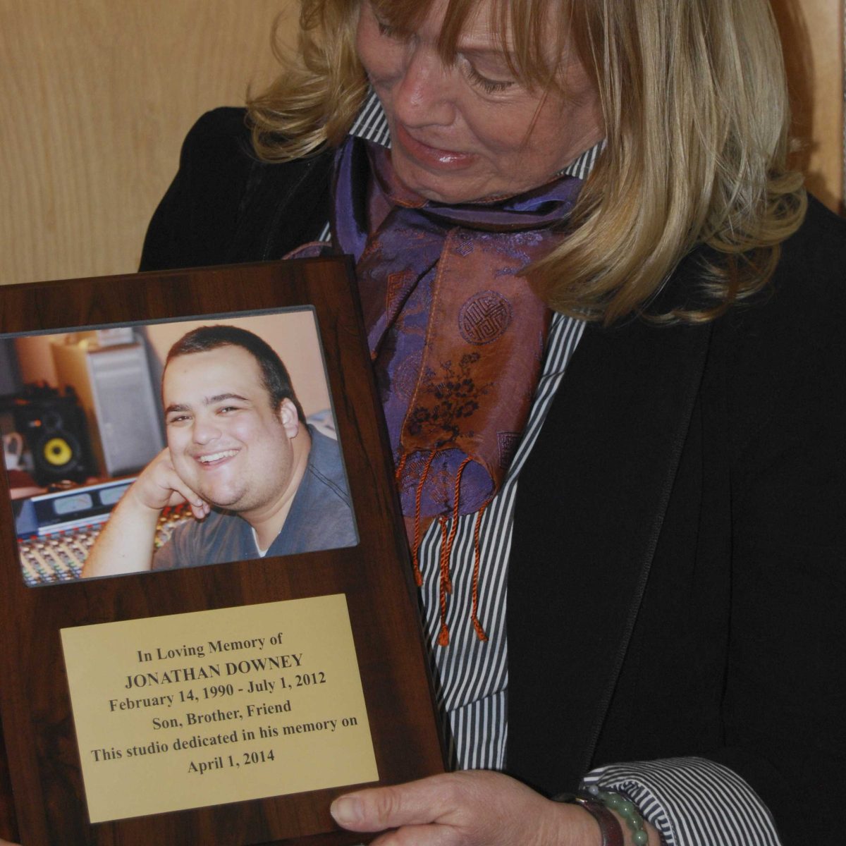 Mary Curran-Downey holds a plague of her deceased son, Jonathan Downey, that will be on display at Palomar College radio station KKSM. (Photo Courtesy of Serena Reid)