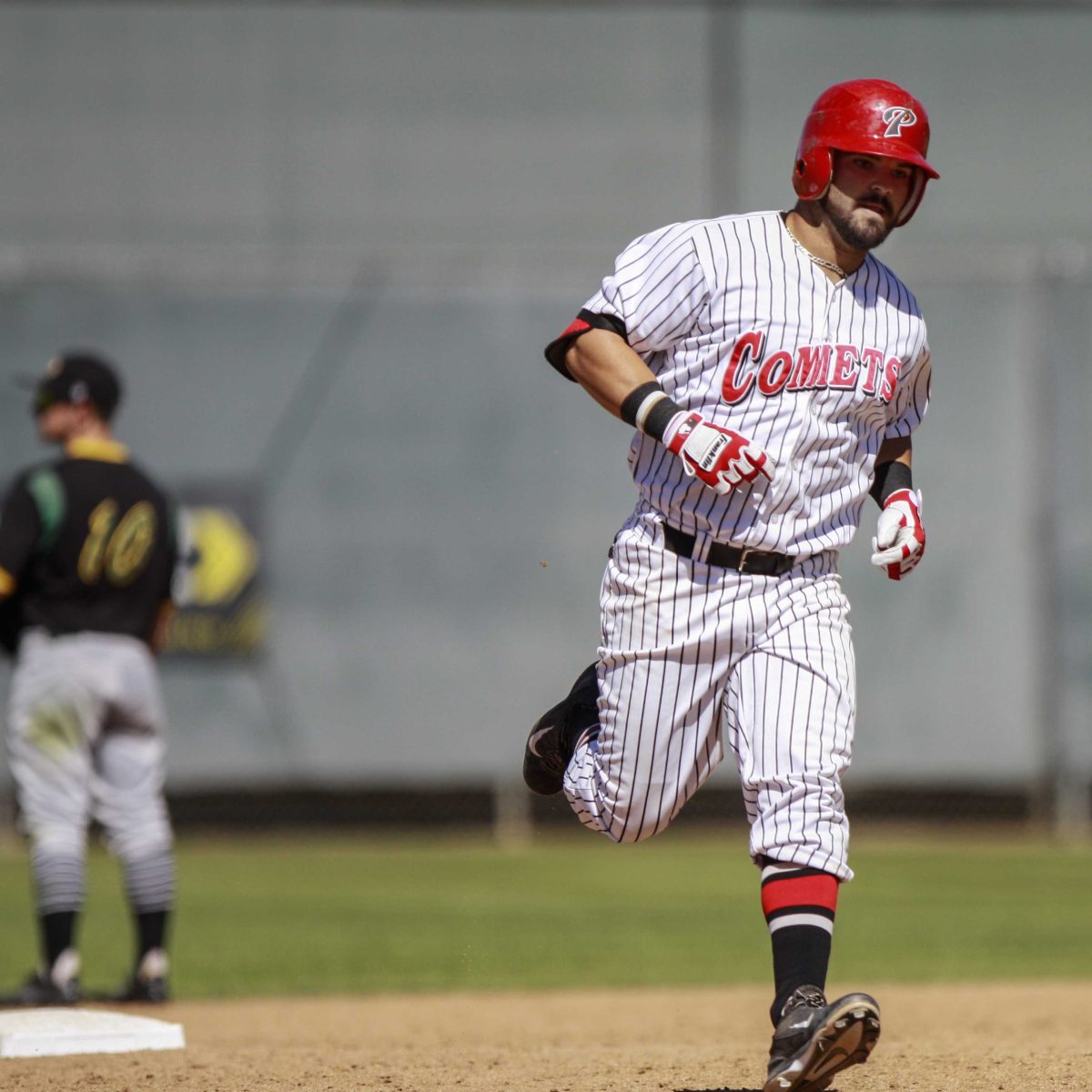 A male Palomar baseball player runs to the right. An opposing players stands in the background to the left, facing the other way.