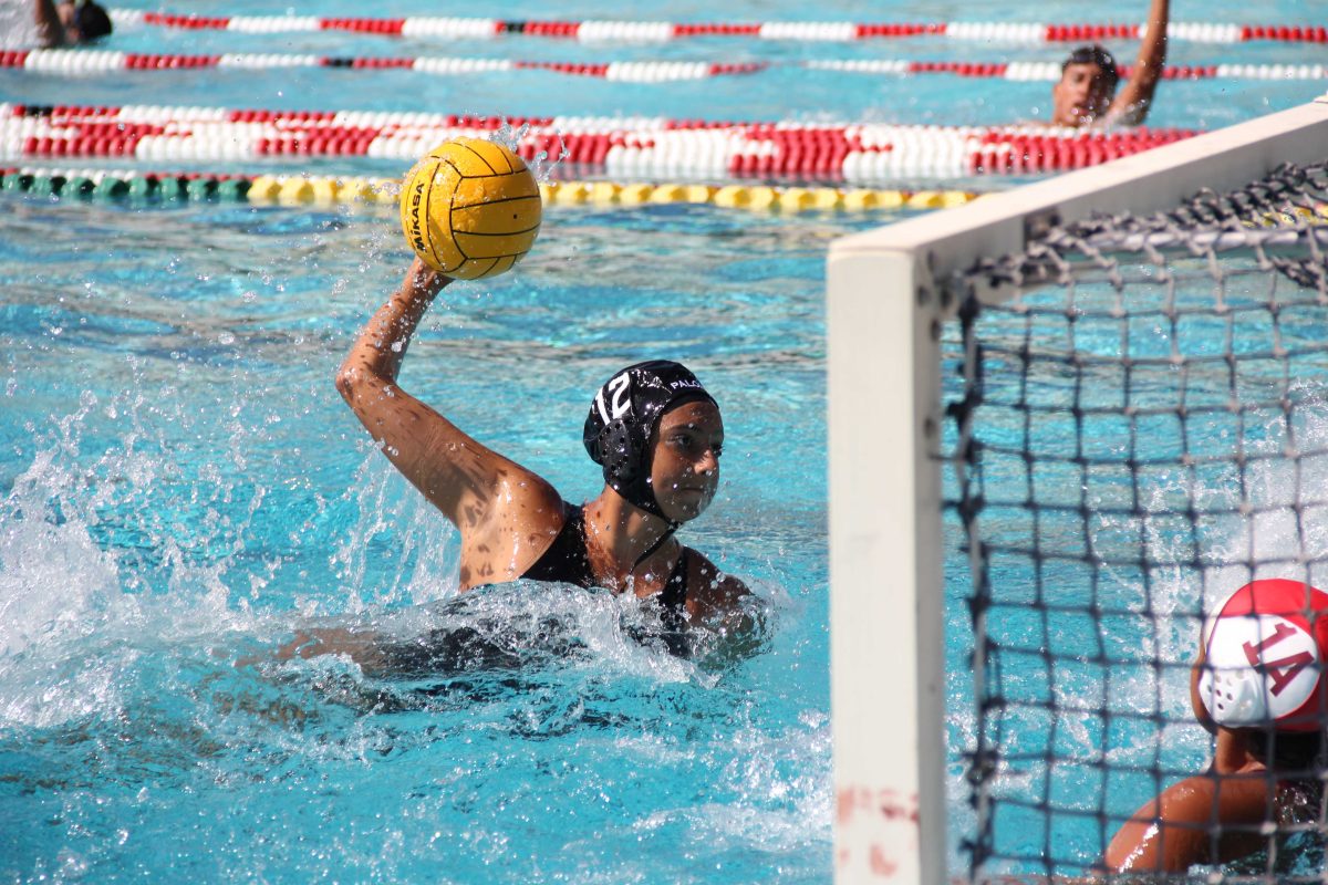 A female Palomar water polo players throws a ball toward a goal.