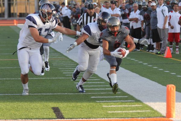 A Palomar football player runs near the sidelines as two opposing players chase him from behind and to his right.