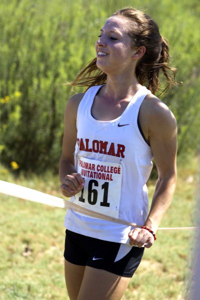 Palomar College Cross Country Invitational at Guajome Park. Sophomore runner and winner Jessica Steinhoff #161, is showing a big smile of pride as she breaks through the finish line tape. Steinhoff remained in the lead throughout the race, several times having a large separation ahead of the other runners. Palomar College Jessica Steinhoff won the race and demonstrated her hard work and pride as a cross country runner. Steinhoff placed first place with a finish time of 20:08.