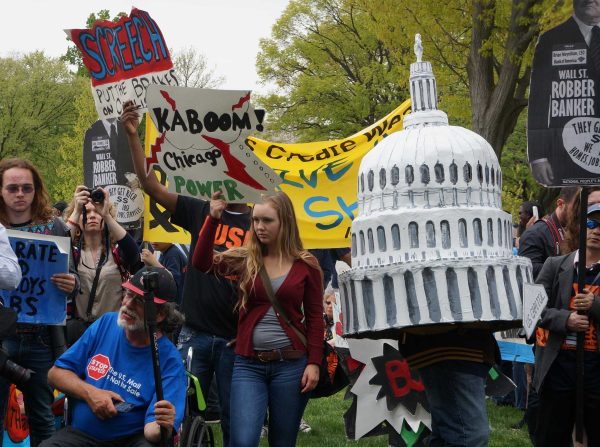 Protestor hold signs and cardboard cut-outs of a "white male banker" and the U.S. Capitol dome.