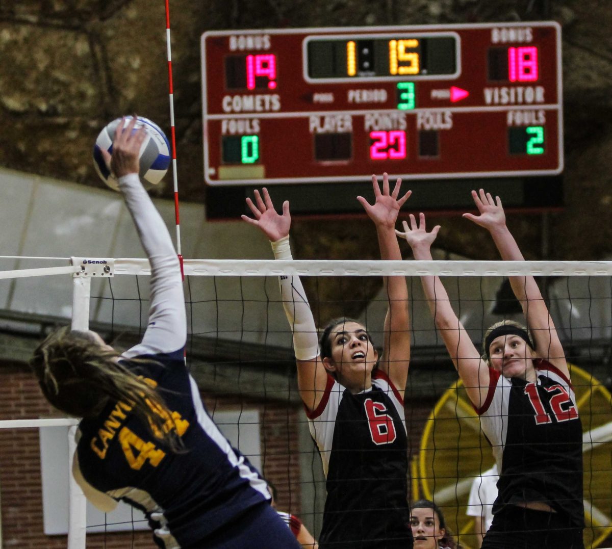 Two female Palomar volleyball players try to block the ball as a opponent spikes it.