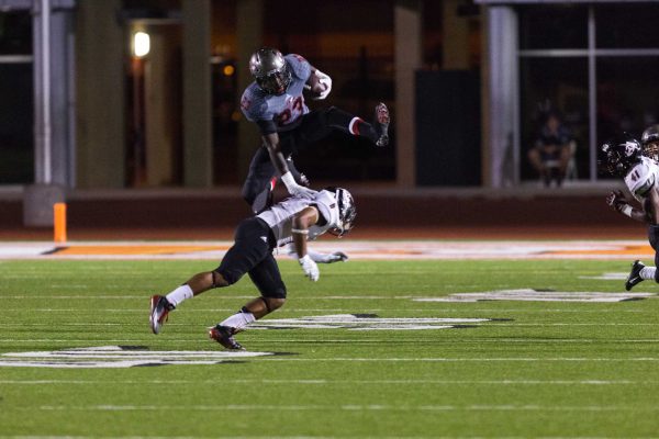 A Palomar football player hurdles over an opposing player while carrying a football in his left arm.