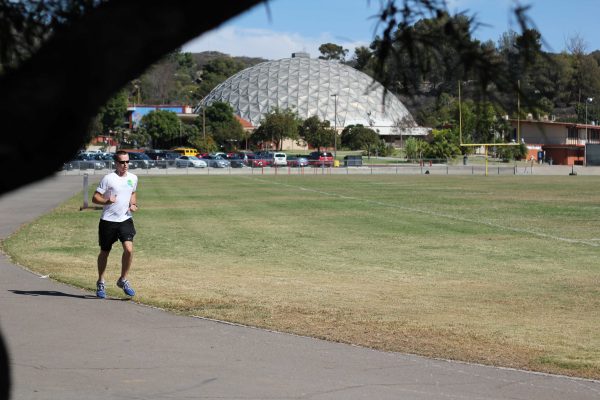A man runs on a track at the football field. The Dome is in the background.