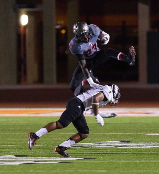 A Palomar football player hurdles over an opposing player while carrying a football in his left arm.