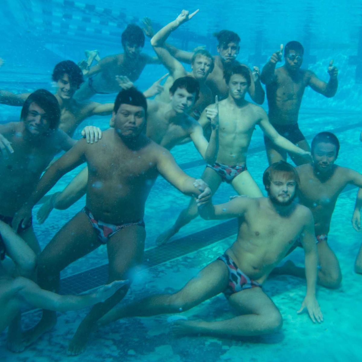 A team of male Palomar water polo players pose underwater at the pool in Speedos.