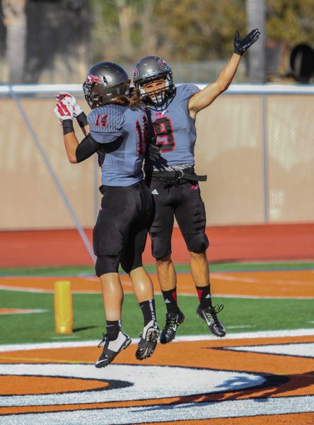 Two Palomar football players jump up and bump each other on their torso in celebration.