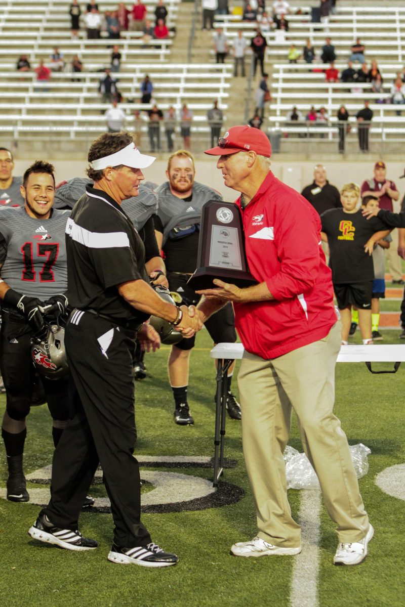 Palomar Athletic Director Scott Cathcart shakes hand with Palomar Head Football Coach Joe Early and holds a trophy in his left hand.