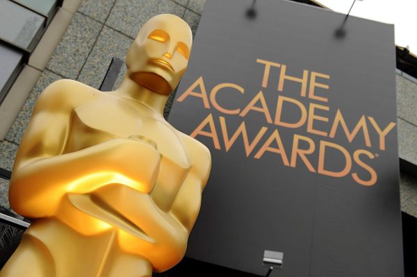 A gold Oscar statue stands on the left with a huge sign "The Academy Awards" hands on the right.