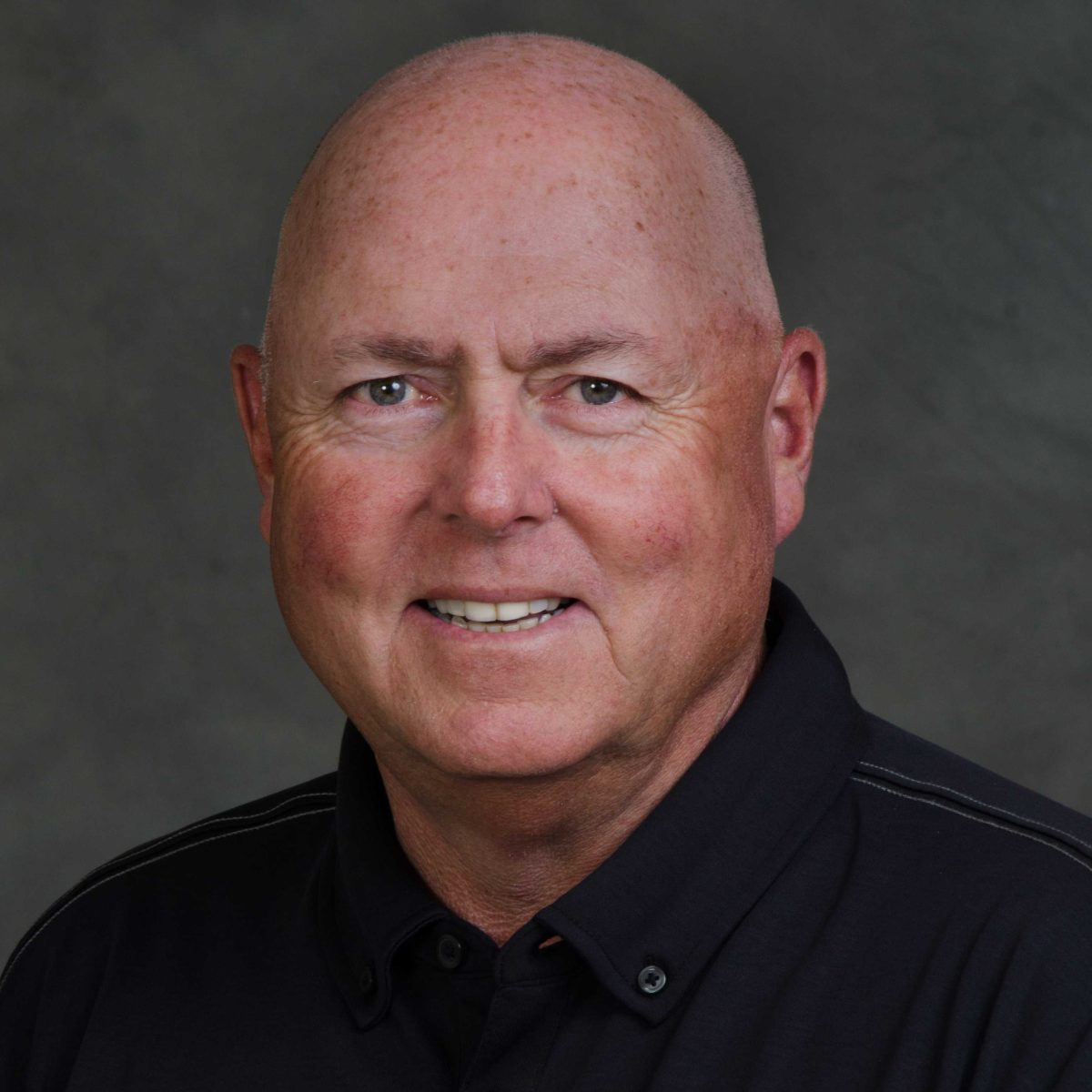 Portrait of women's golf coach Mark Halda. He wears a black polo shirt.