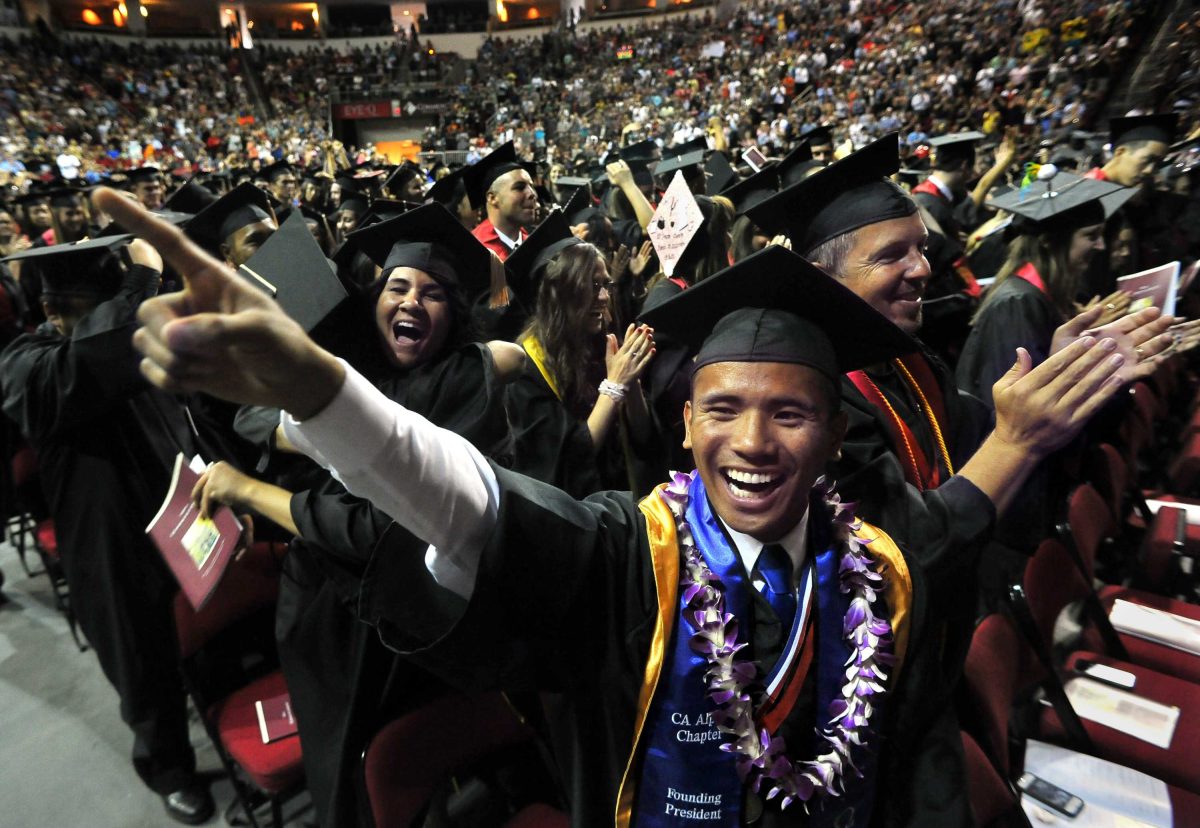 A huge group of people wearing a black cap and gown celebrates their graduation in a stadium.