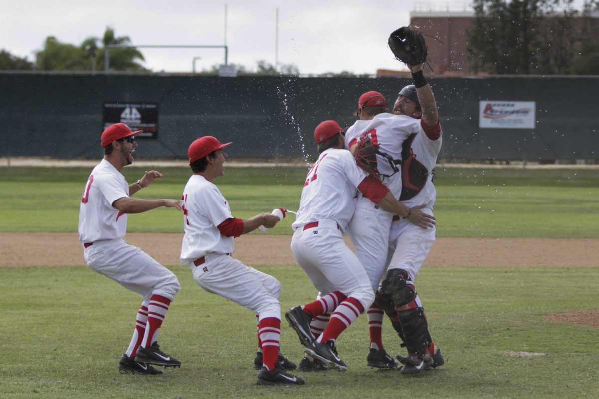 Three Palomar baseball players hug each other as two other players behind them laugh. One of them squirts water from a water bottle at one of the huggers.