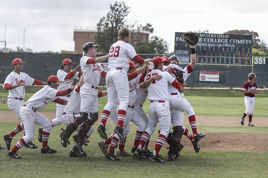 A group of Palomar baseball players hug each other. Two of them jump in the air in excitement. An opposing player walks on the right slightly in the background looking in the opposite direction.