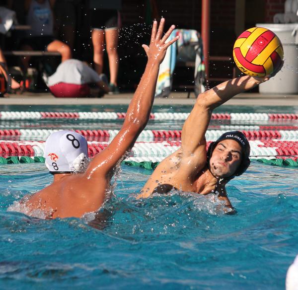 A male Palomar water polo player tries to throw a ball from as an opponent tries to block him with his left arm.