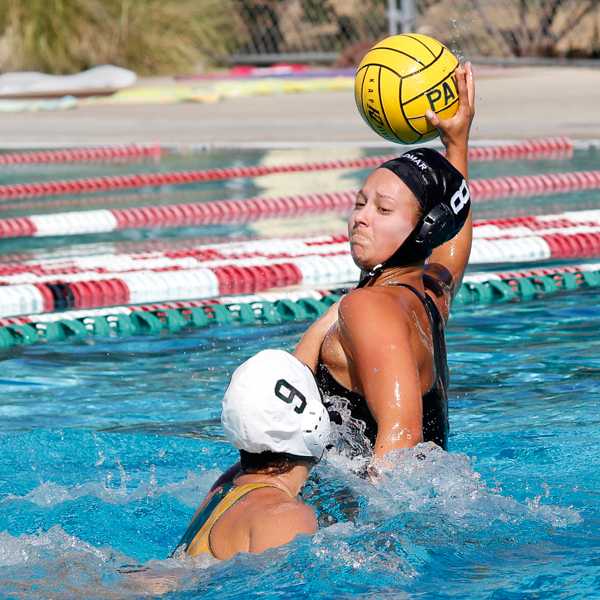 A female Palomar water polo player tries to throw the ball in her right hand as an opponent tries to block her from the left.