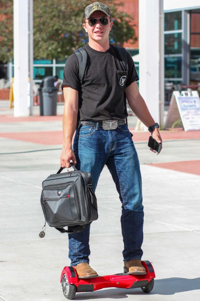 A male Palomar student rides on a red hoverboard while carrying a grey laptop bag in his right hand.