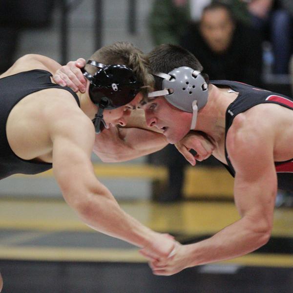 Two male wrestlers grapple each other while their foreheads touch. They both wear earguards.