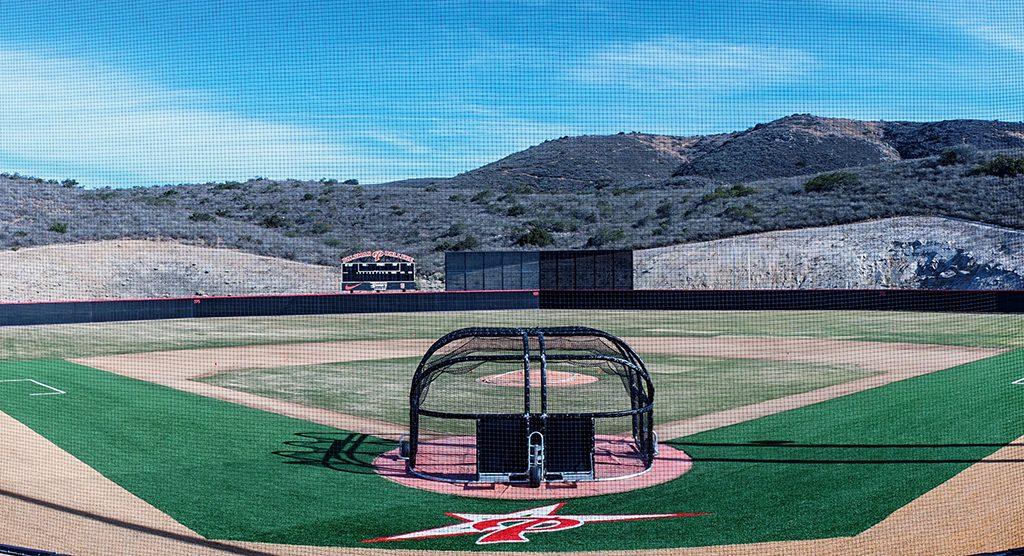 Palomar College's new baseball field with the battle cage in the foreground and a scoreboard in the background. Hills covered with dry brush are in the background.