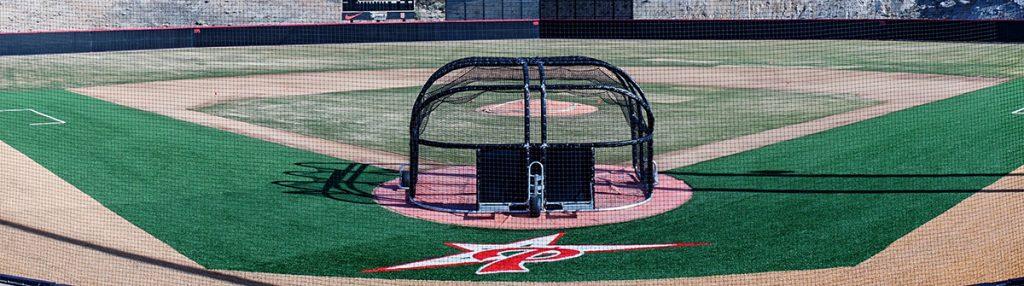 Palomar College's new baseball field with the battle cage in the foreground and a scoreboard in the background. Hills covered with dry brush are in the background.