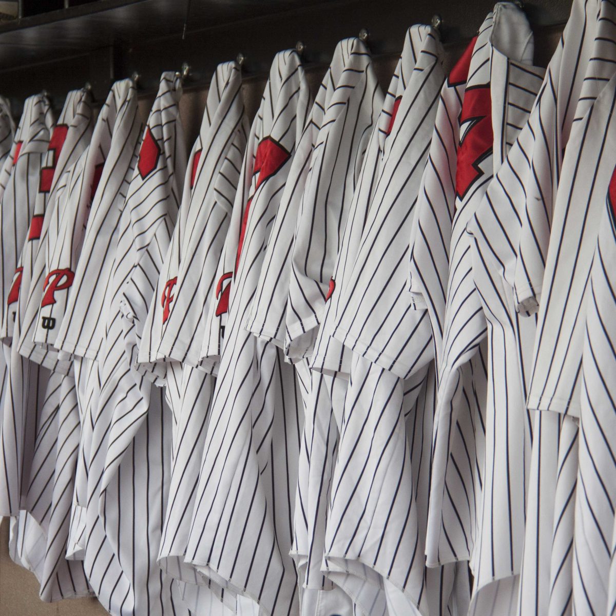 Palomar baseball team uniforms, white with thin vertical black stripes, hang in the dugout.