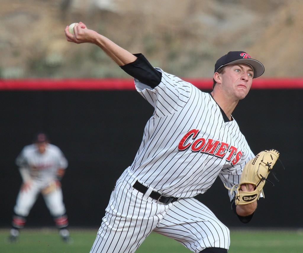 A male Palomar baseball player throws a baseball with his right hand. A teammate stands in the background in the outfield (blurry).