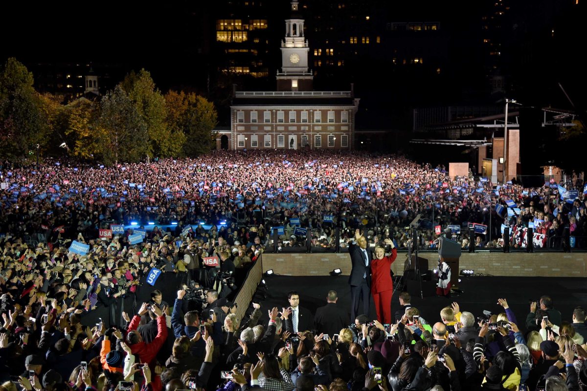 A huge crowd gathers around a stage at night with former president Barack Obama and Hillary Clinton on it.