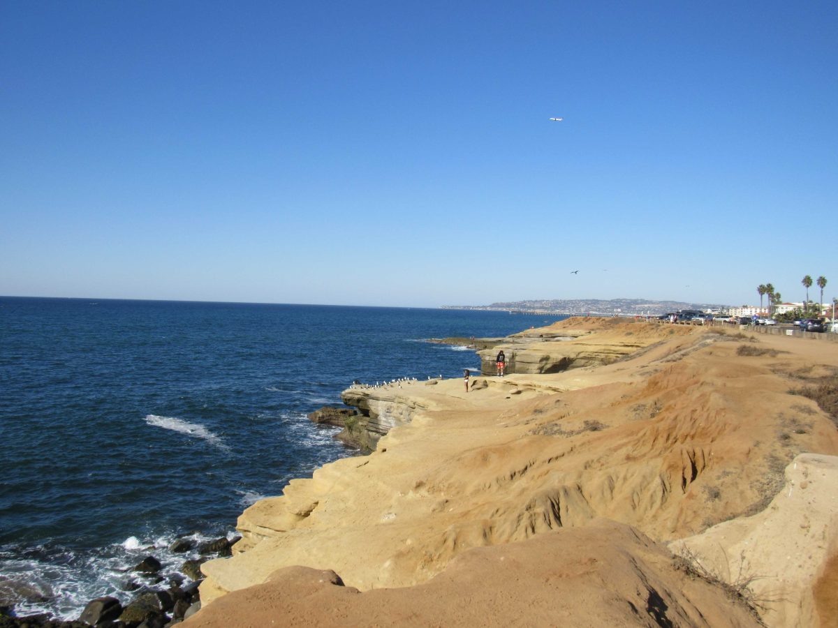 Sandy cliffs line with the ocean shore. Two people are on a cliff with seagulls.