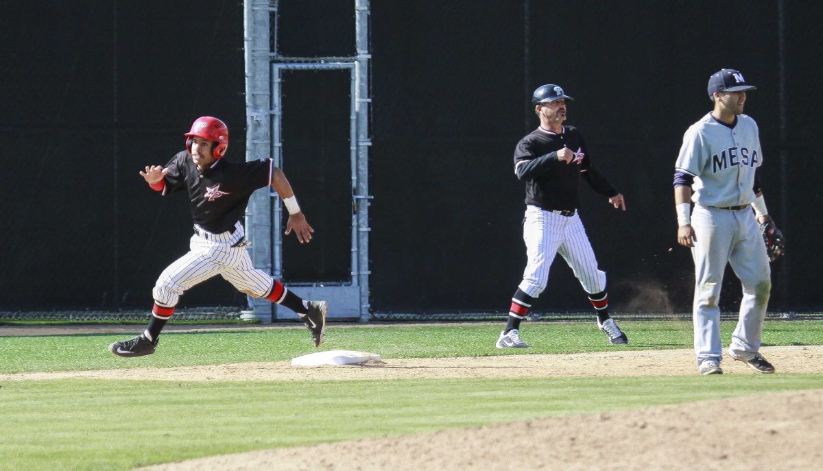 A male Palomar baseball player runs on the left as a teammate and an opposing players stands and watch to the right.