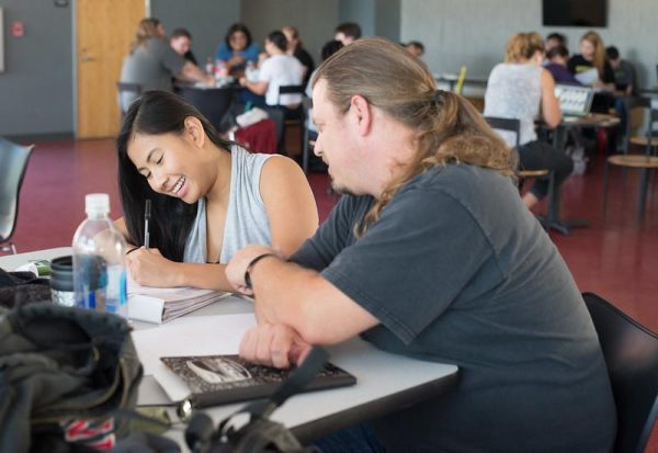 A man with dark blonde hair and woman with black hair do their homework at a table at Palomar's cafeteria.