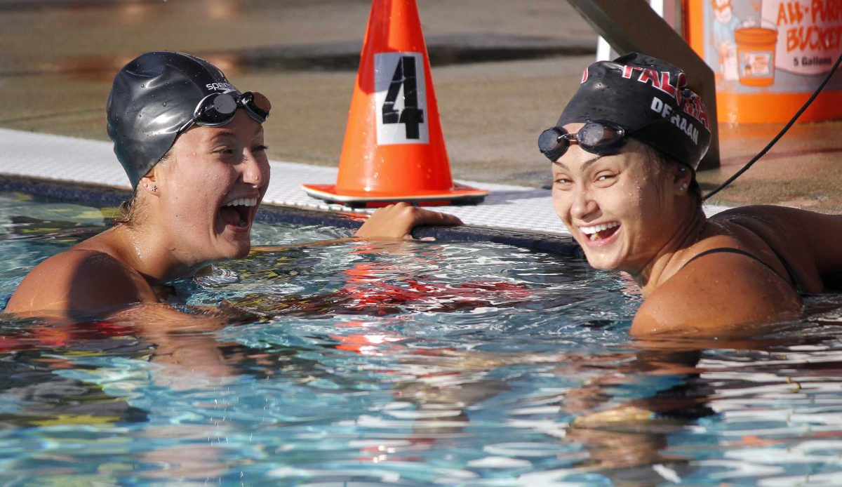 Two female Palomar swimmers laughs in the pool near the edge.