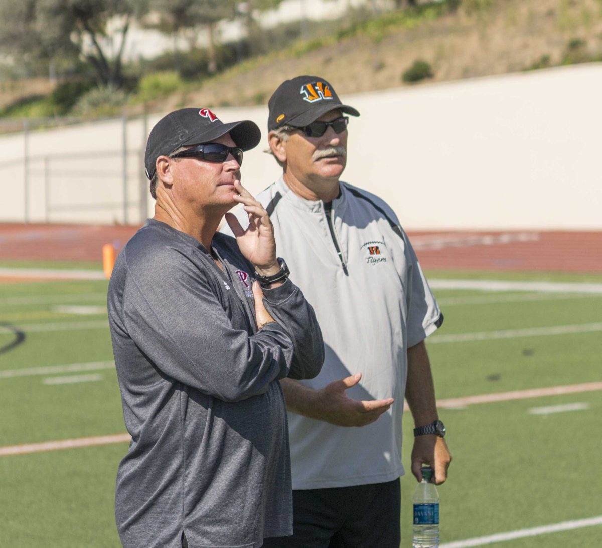 Palomar coach Joe Early (left) and Riverside City College coach Tom Craft (right) stand next to each other and talk on a football field.