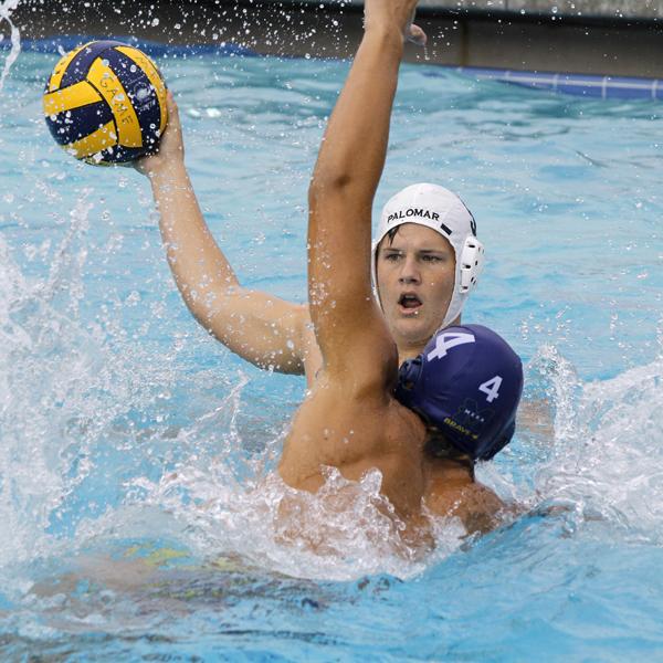 A male Palomar water polo players throws a ball with his right hand as an opponent tries to block with his left arm.