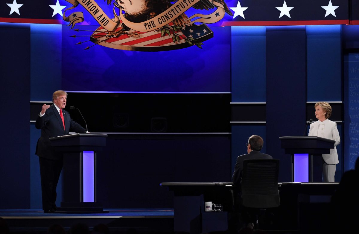 Donald Trump stands at a lectern on the left, and Hillary Clinton stands at a lection on the right. A male moderator sits in the middle.